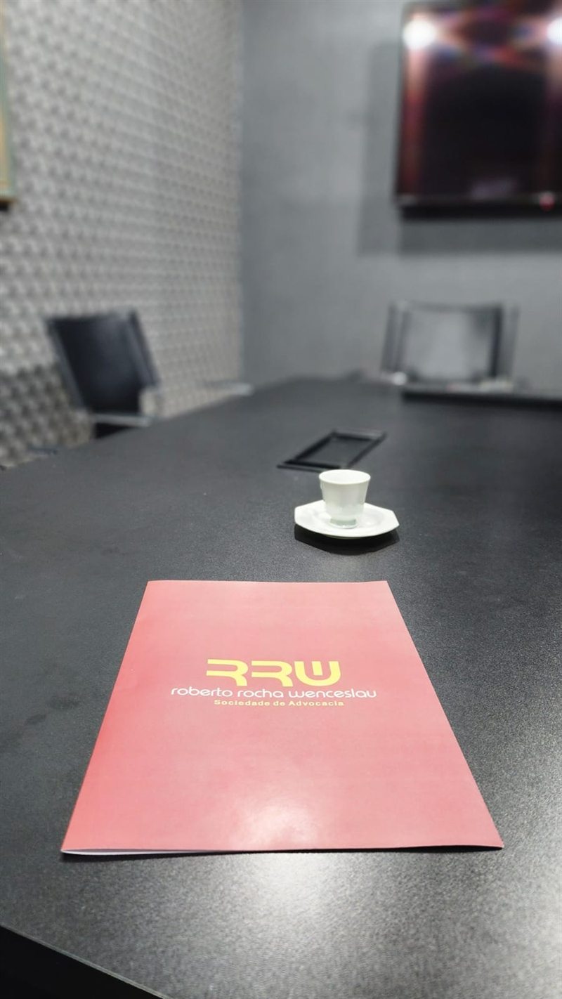 Mesa de reuniões do escritório, com a pasta institucional RRW e um café servido ao cliente